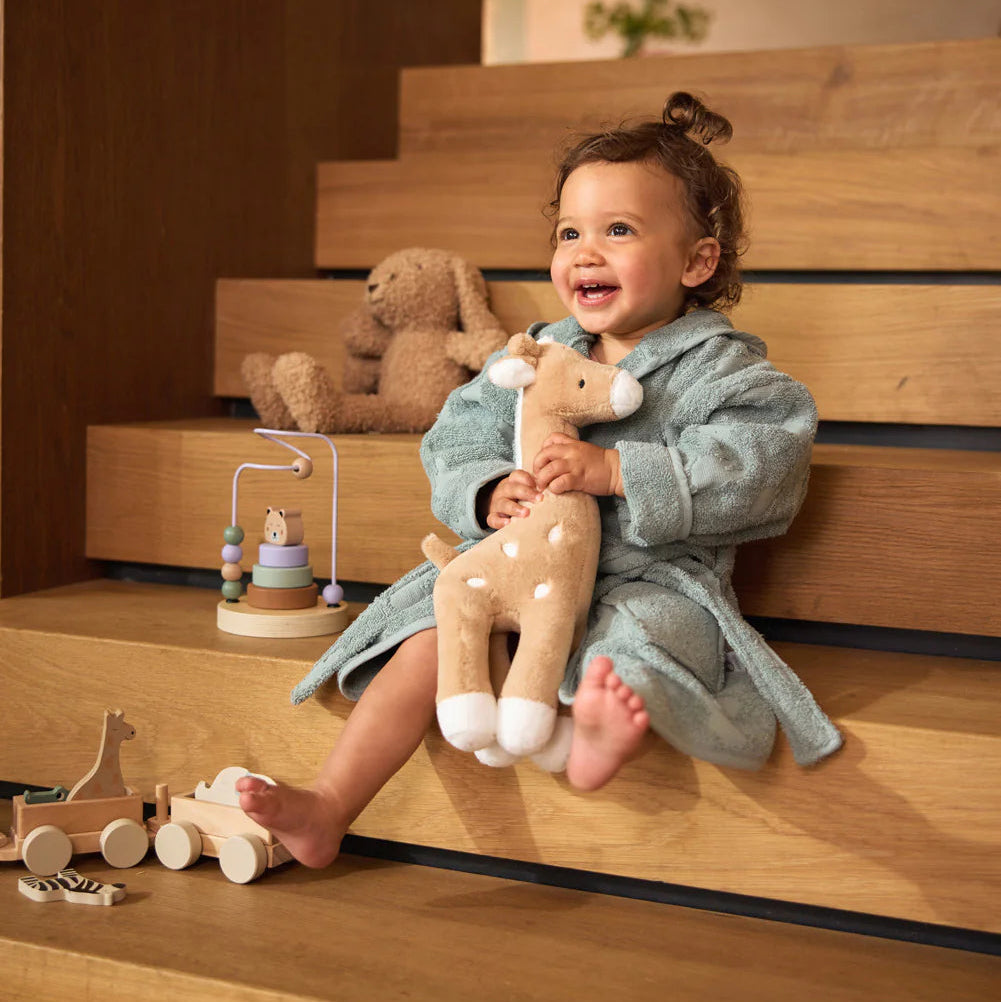 Child in a bathrobe holding a plush toy on wooden stairs
