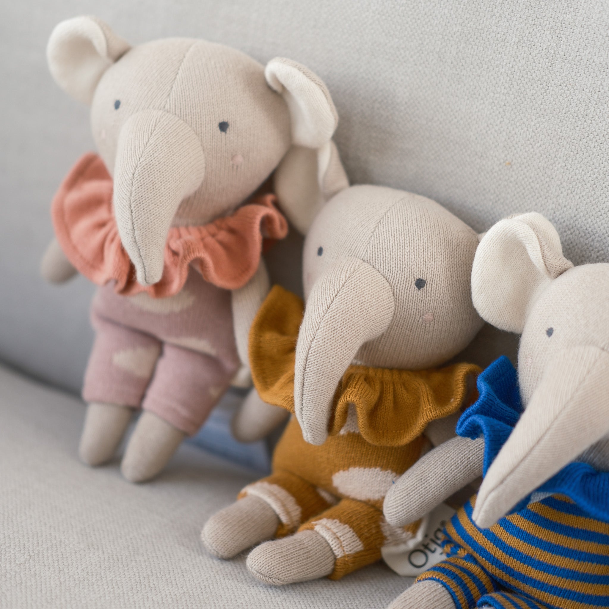 Three plush elephant toys in different colors and outfits on a light gray background