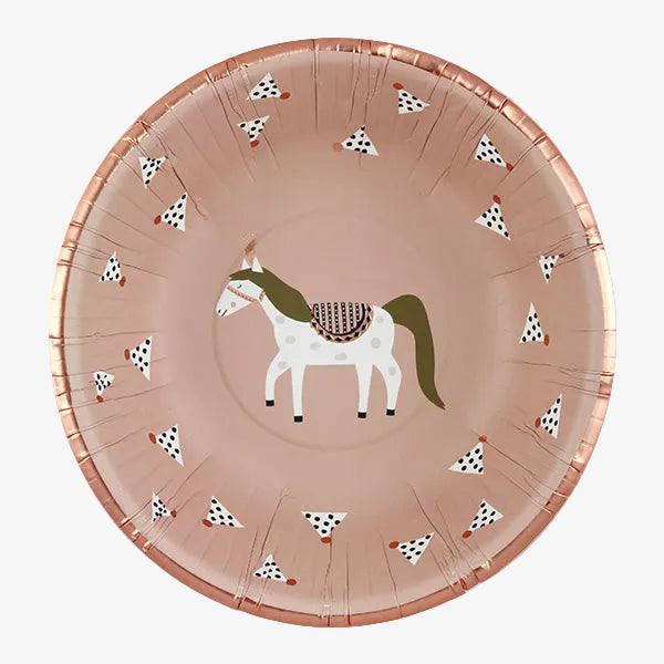 A round paper party plate in a dusty rose pink color, decorated with a central illustration of a white horse with a green mane and tail, and small black-and-white spotted motifs around the rim.