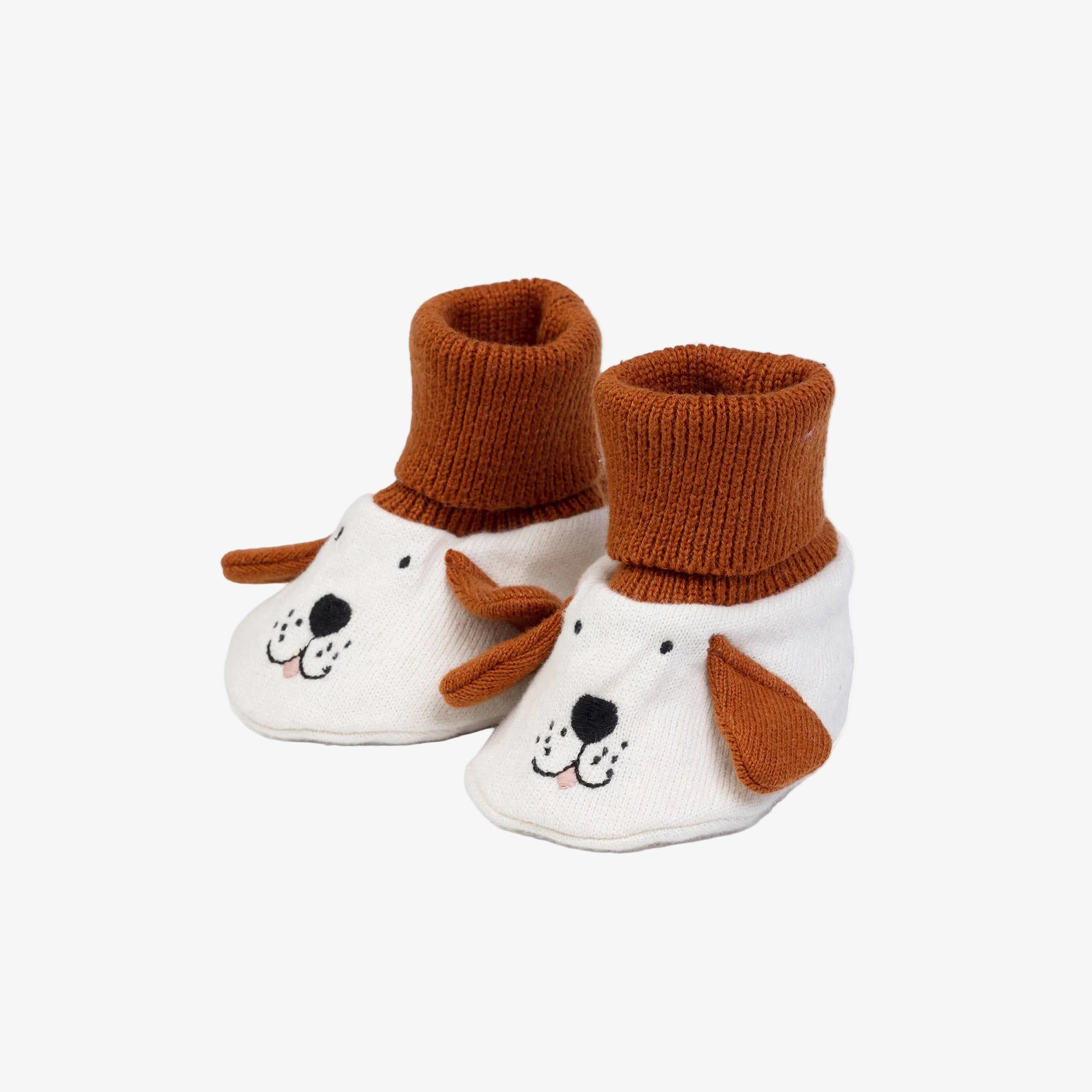 A pair of baby booties designed to look like a dog's face, featuring white knit uppers with embroidered black facial details, brown knit ears, and brown knit cuffs.
