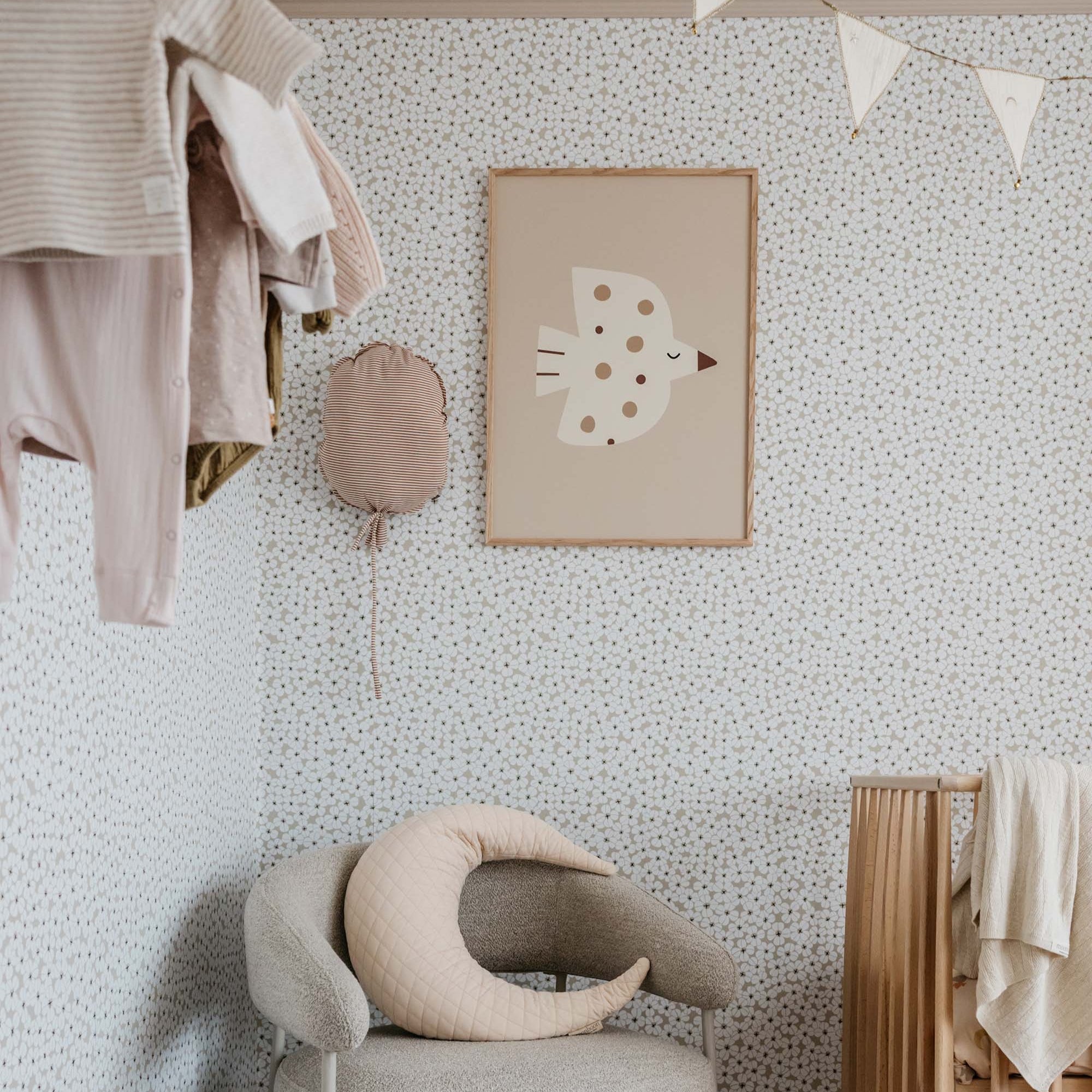 Nursery room with a chair, crib, and little otja poster with bird and oak wooden frame on a patterned wallpaper.