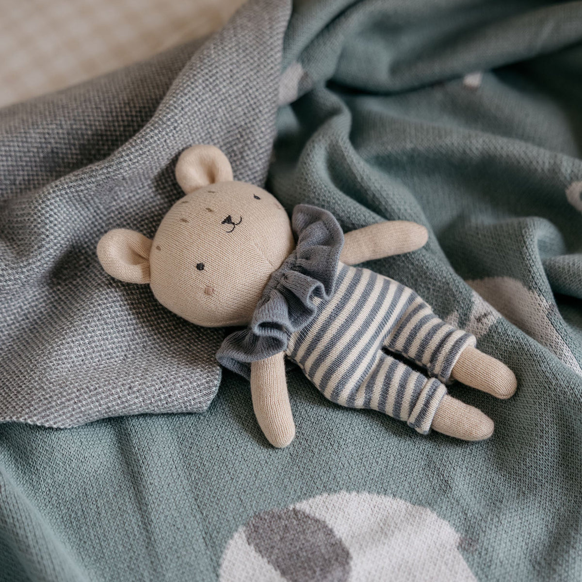 Stuffed teddy bear in a striped outfit on a soft blanket with elephant design