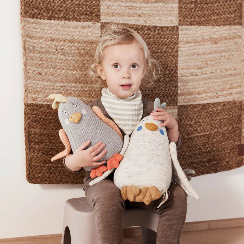 Child sitting on a stool holding two plush toys against a textured wall.