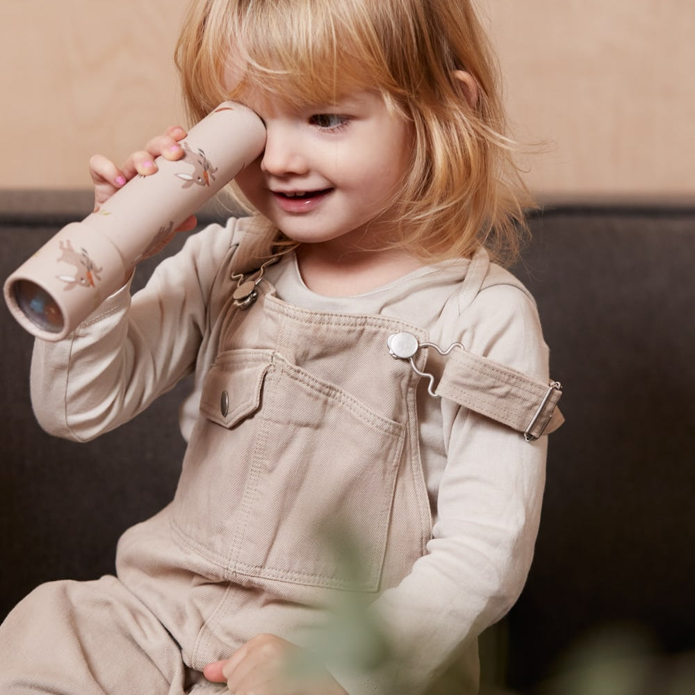 Child in beige overalls holding a toy phone against a neutral background 