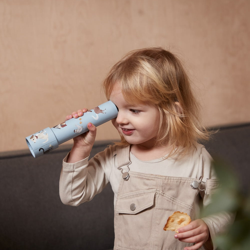 Child holding a toy telescope and a cookie, standing against a neutral background 