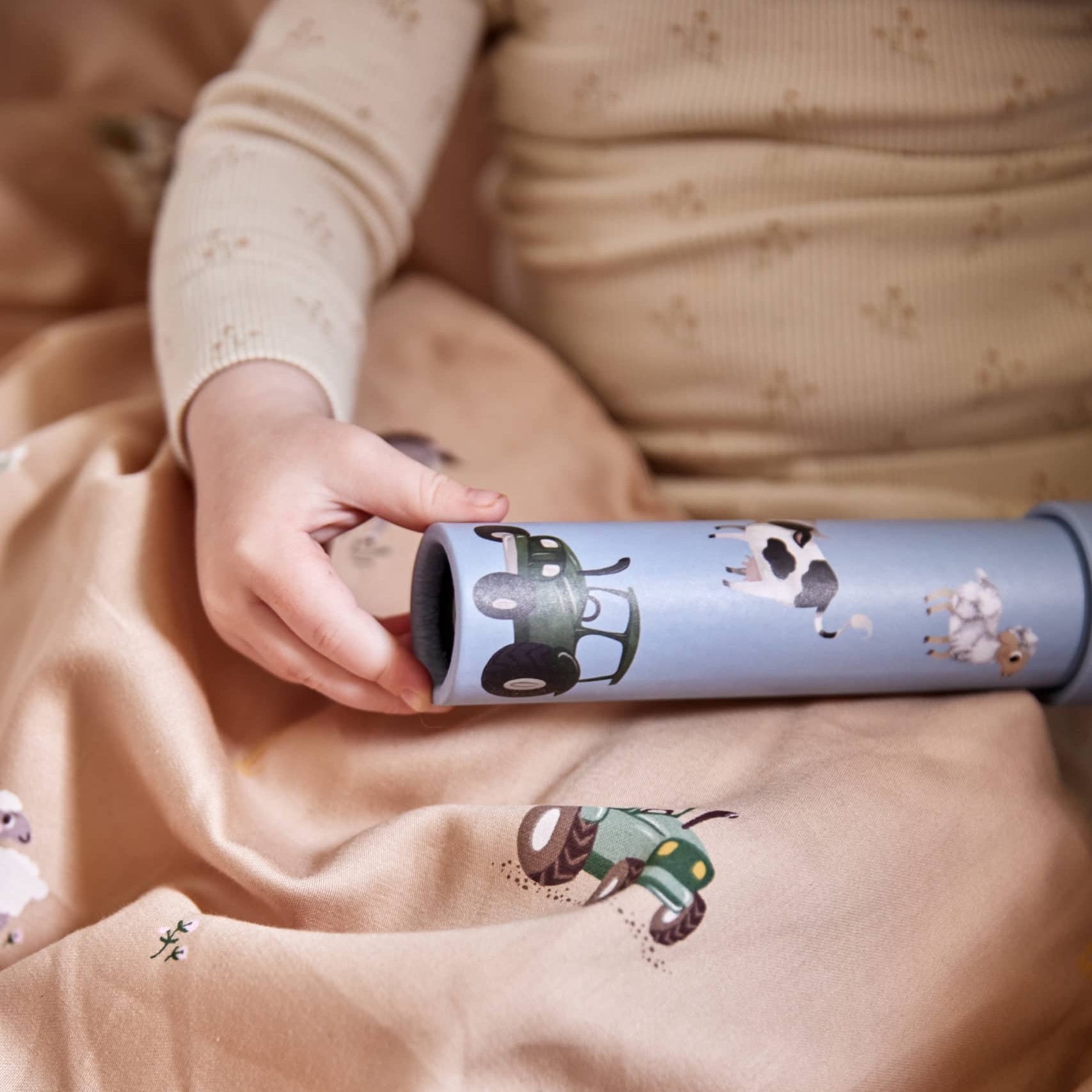 Person holding a cylindrical toy with cartoon characters on a beige blanket.