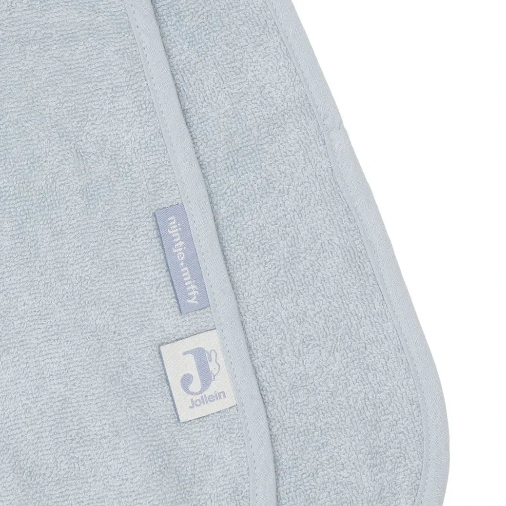 A close-up of a light blue-gray textured fabric, likely a towel or blanket, with a folded edge showing a small vertical fabric tag and a square brand patch. The tag reads 'jassen' and the brand name 'Jassen' is visible on the square patch. 