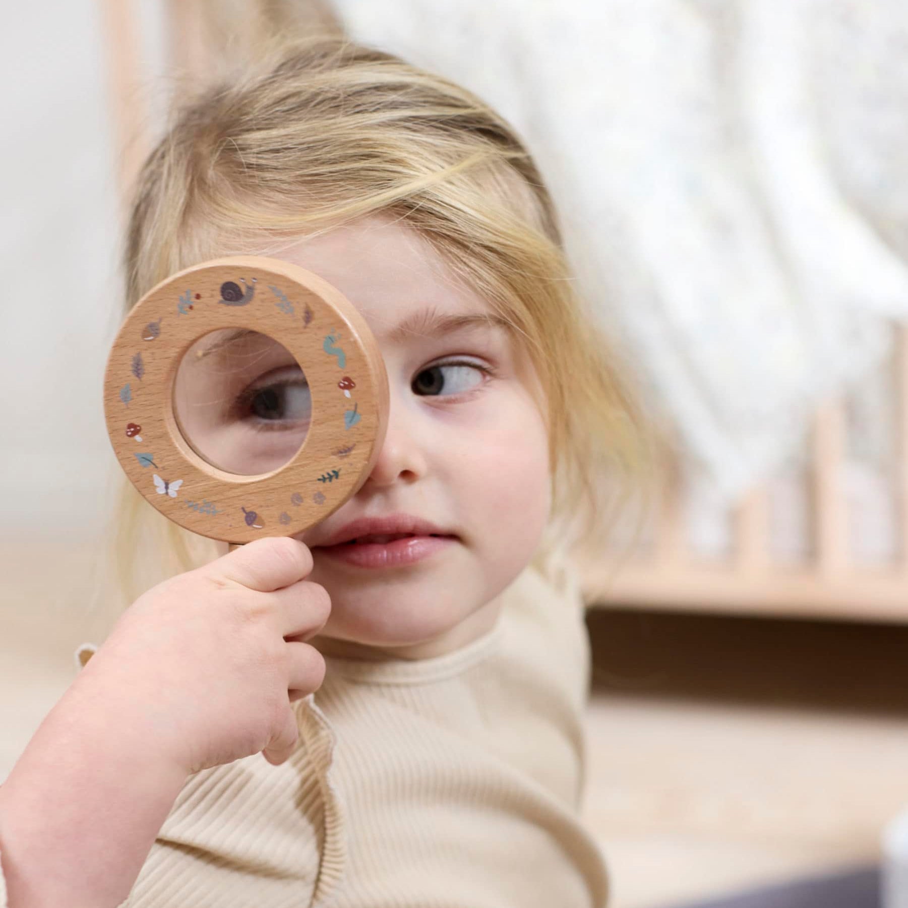 Child holding a wooden toy near their face in a softly lit room.