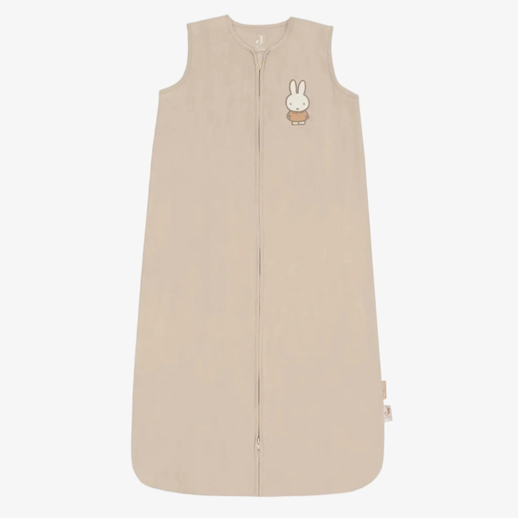 A sleeveless baby sleep sack in a light beige color, featuring a front zipper, a small embroidered cartoon bunny on the left chest, and a small fabric tag on the lower right hem, shown against a plain white background.