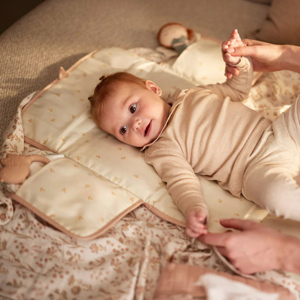 Baby lying on a soft surface with a person's hand holding their foot