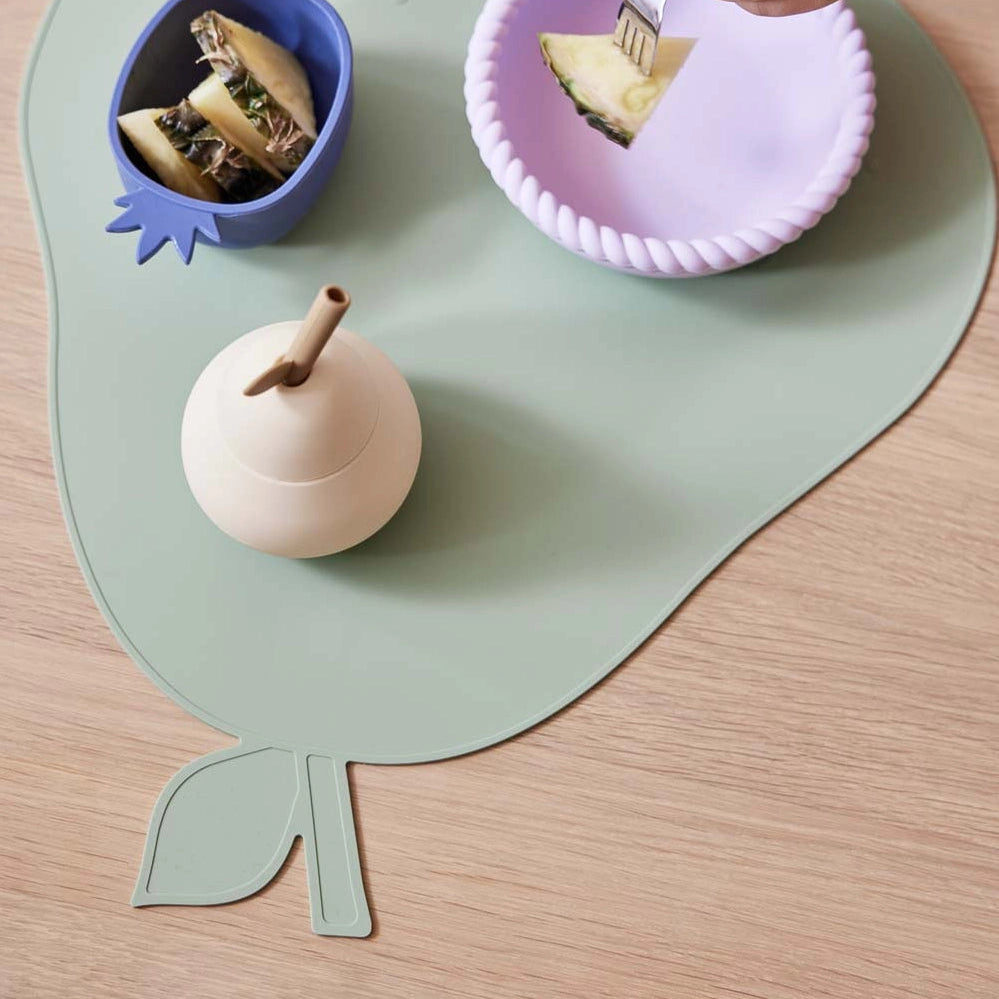Children's table setting with leaf-shaped placemat, colorful bowls, and toys on a wooden surface.
