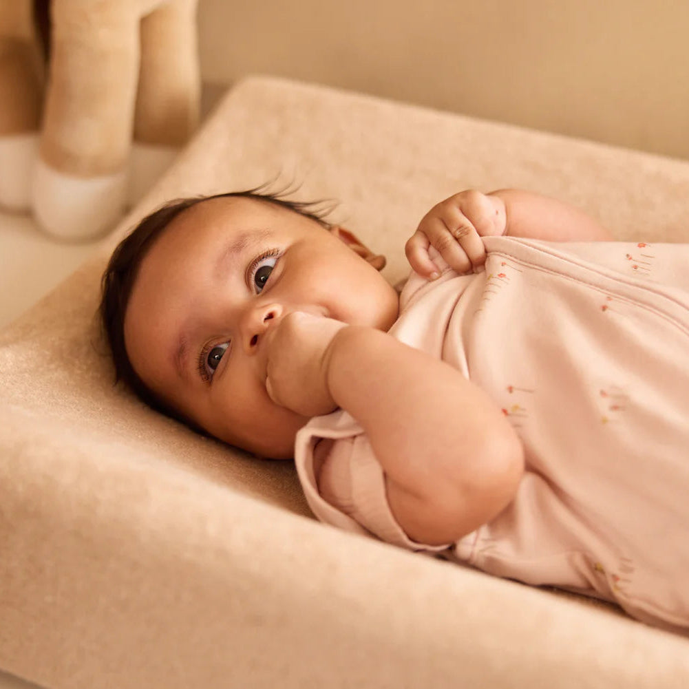 Baby lying on a beige changing pad with a soft focus background
