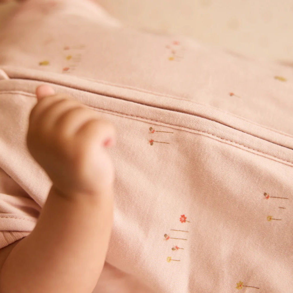 Close-up of a baby's hand on a pink garment with floral patterns.