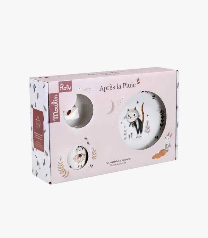 A boxed set of ceramic dishes by Roby, featuring a light pink package with illustrations of a cat, bunny, moon, and leaves, plus a circular cutout showing part of the white plate set inside.