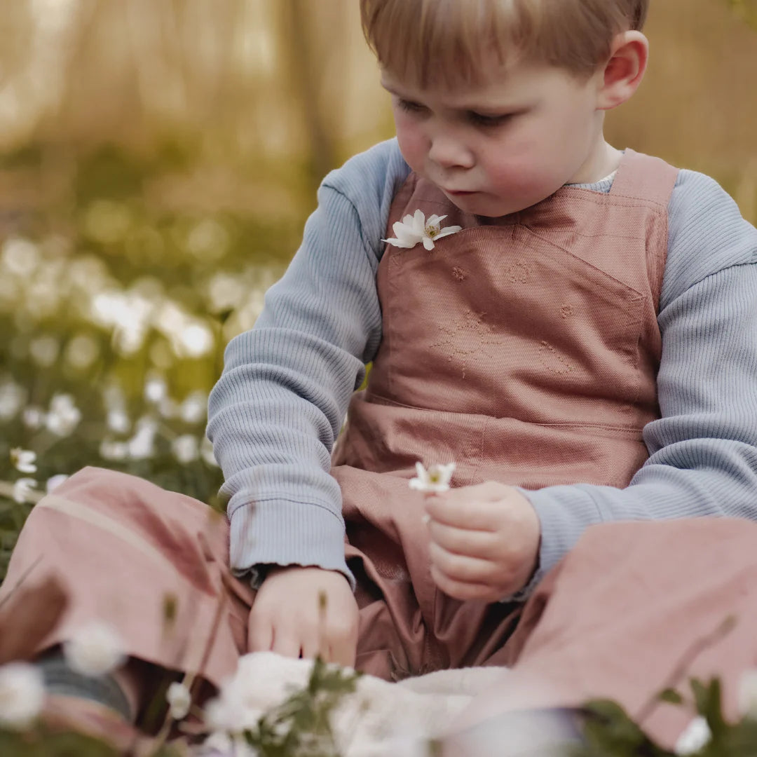Child in a pink dress sitting outdoors with flowers