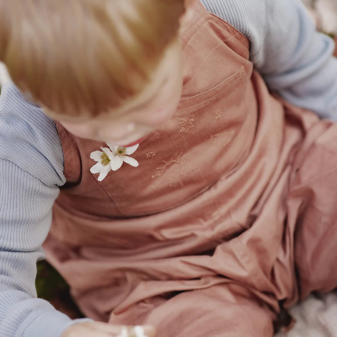 Child wearing pink overalls with a white flower on a blurred background