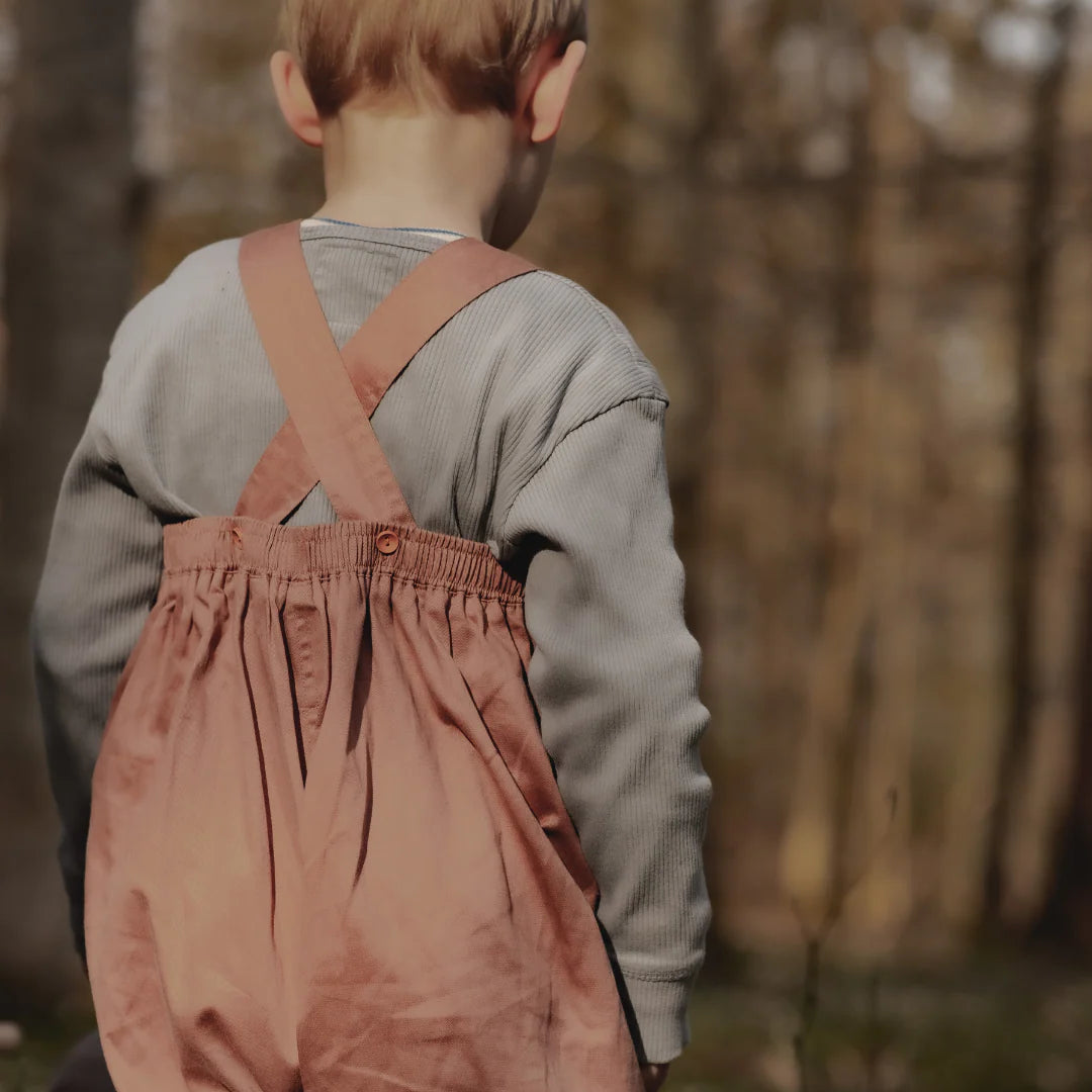 Child wearing pink overalls walking away in a natural setting
