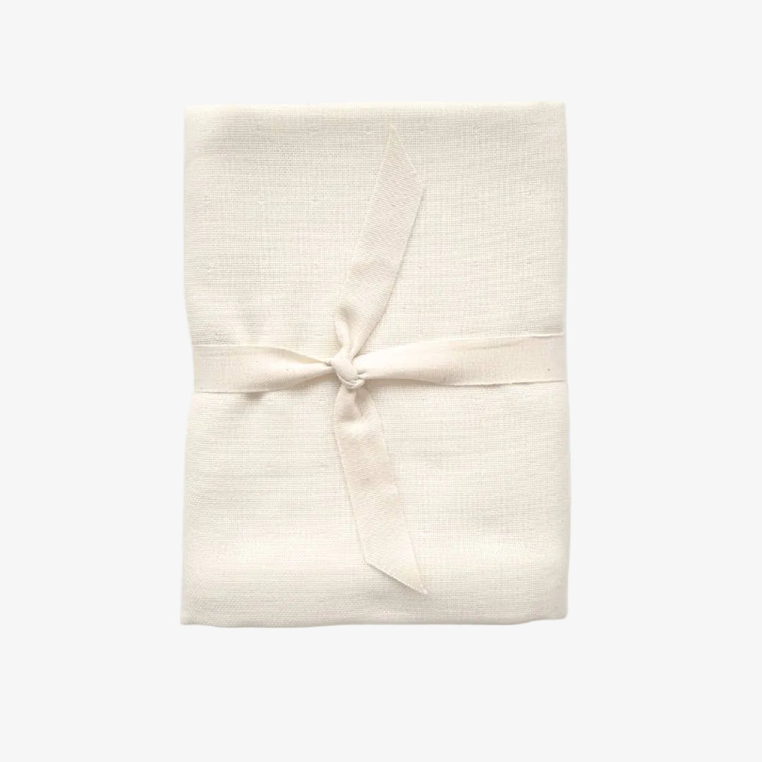 A folded cream-colored cotton muslin cloth tied with a matching ribbon bow, presented on a clean white background.